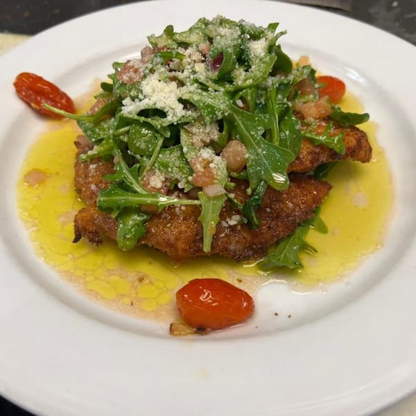 Monalisia's breaded chicken cutlet topped with arugula, diced tomatoes, and grated cheese, drizzled with olive oil.