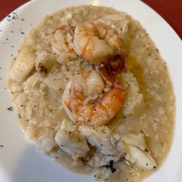 Creamy seafood risotto with shrimp and scallops, garnished with herbs on a white plate.