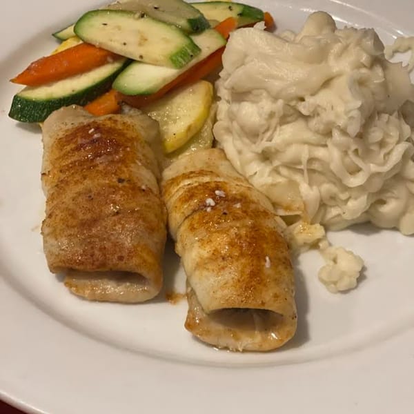 Two rolled fish fillets with roasted zucchini, carrots, and mashed potatoes on a white plate.