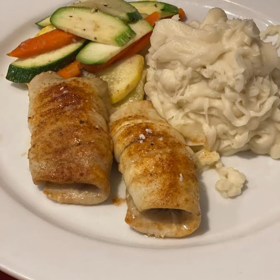 Two rolled fish fillets with roasted zucchini, carrots, and mashed potatoes on a white plate.