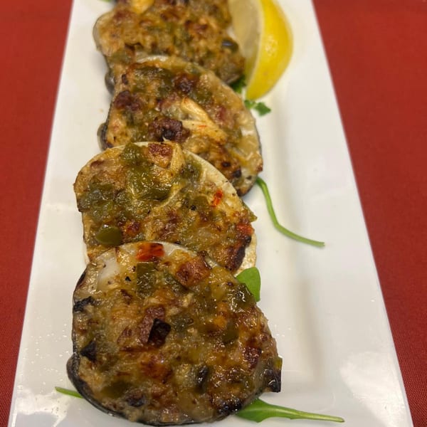 Four baked clams with green and red peppers, garnished with a lemon wedge and arugula.