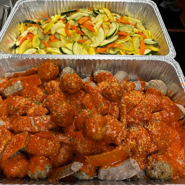 Two catering trays, one with sautéed zucchini and carrots, the other with meatballs and sausage in red sauce.