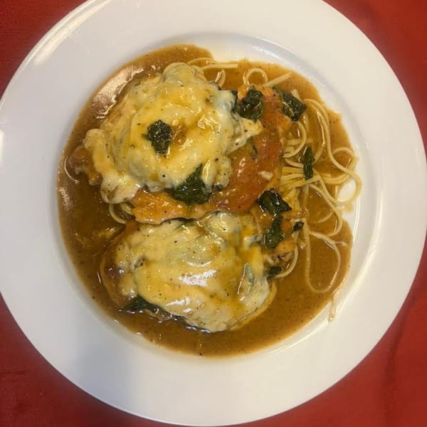 Monalisia's chicken dish with melted cheese, spinach, and spaghetti in a rich sauce on a white plate.