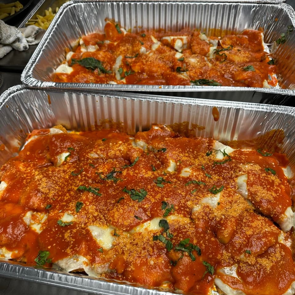 Two aluminum trays filled with Monalisia's baked Italian manicotti, topped with red sauce, cheese, and herbs.