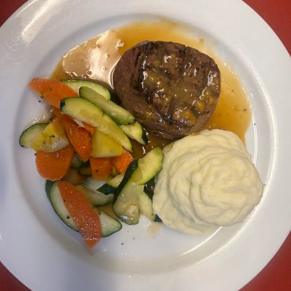 Monalisia's Italian dish features steak with gravy, mashed potatoes, and sautéed zucchini and carrots.