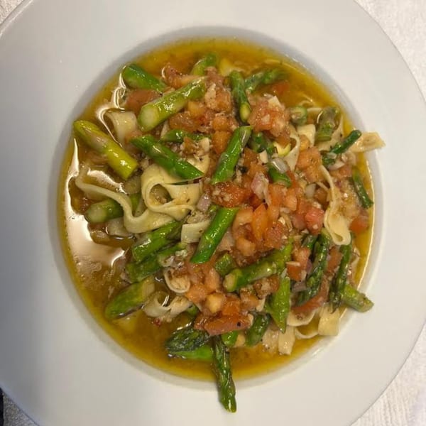 Monalisia's Italian pasta dish with asparagus, diced tomatoes, and a light sauce in a white bowl.