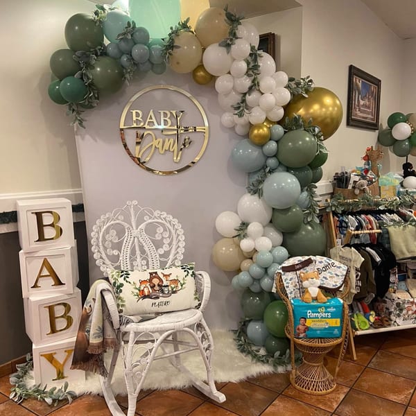 Baby shower decorations with a balloon arch, "Baby Dante" sign, and baby clothes display.