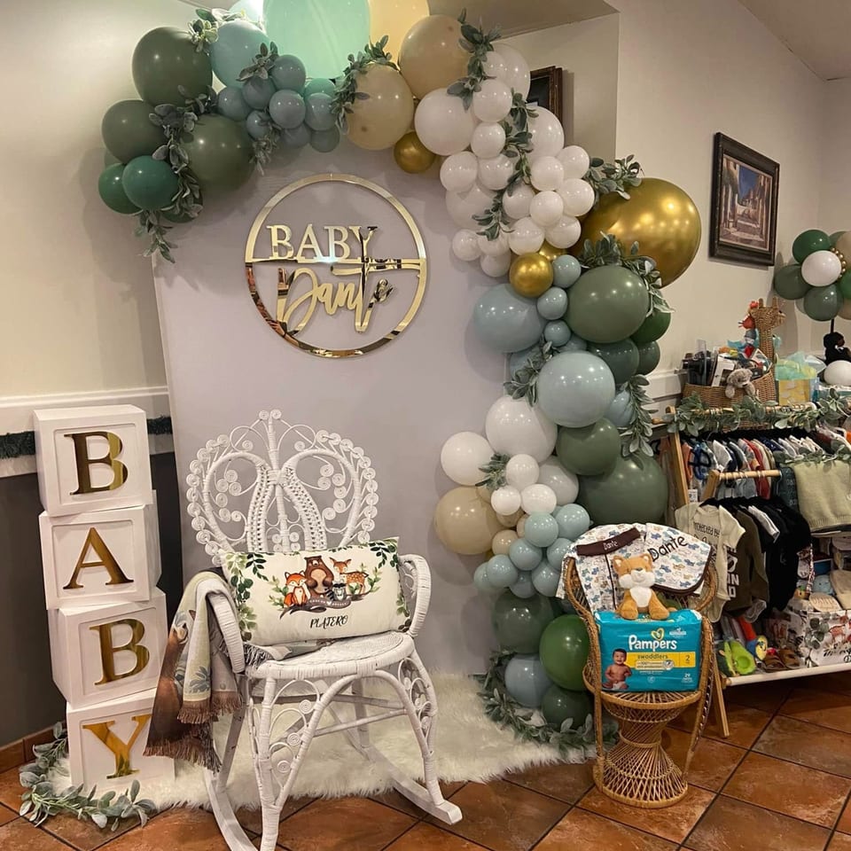 Baby shower decorations with a balloon arch, "Baby Dante" sign, and baby clothes display.