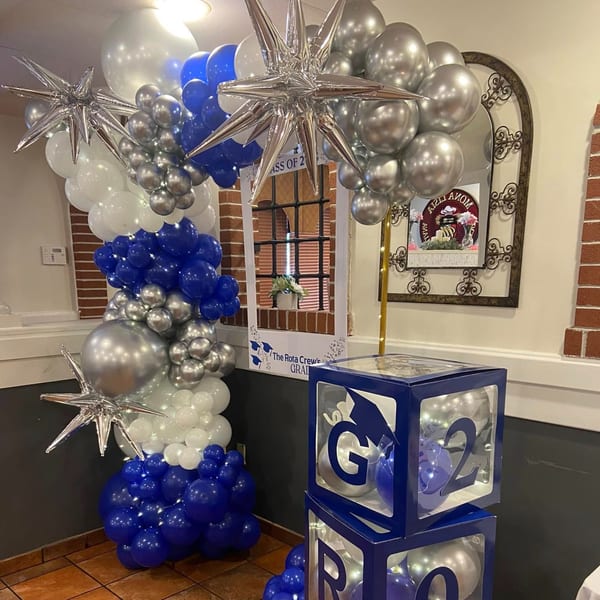 Blue, white, and silver balloons form an arch with star accents, next to graduation-themed decor.